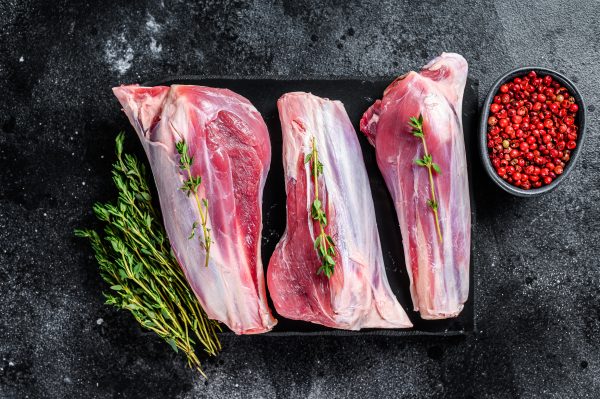 Raw goat shanks meat on a marble board. Black background. Top vi